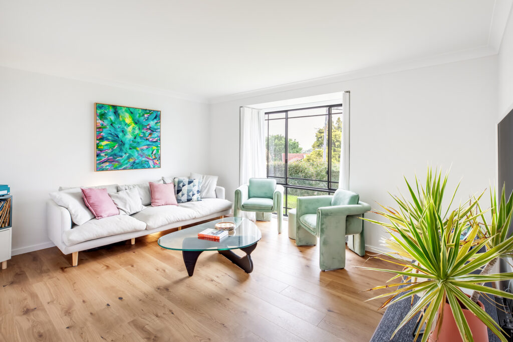 A contemporary living room in Freshwater designed by Hoverco, featuring elegant green accent chairs, a white sofa, and natural light from large windows.