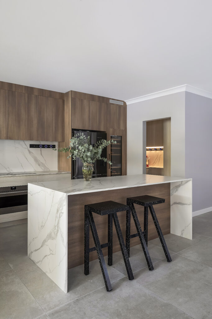 A custom wood-finish kitchenbuilt by Hoverco, featuring a marble island, black appliances, and stylish lighting.