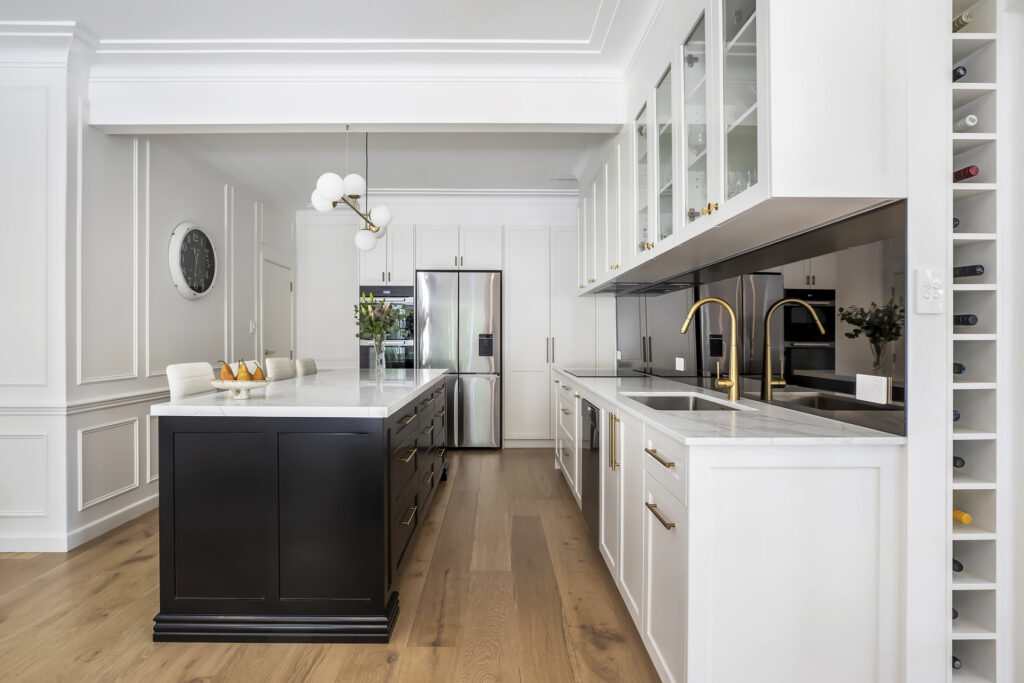 A luxury kitchen renovation by HoverCo, featuring a striking black and white island, gold fixtures, glass cabinetry, and a sleek mirrored splashback for a high-end modern design.
