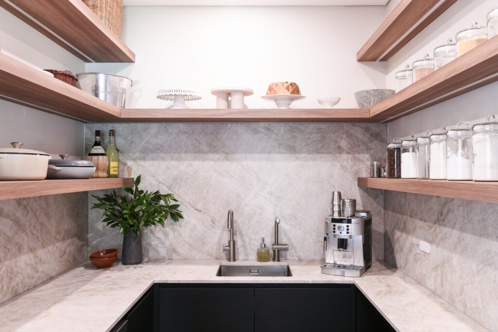 A stylish and functional butler’s pantry designed by HoverCo, featuring open wood shelving, a marble backsplash, black cabinetry, and a built-in sink for a luxurious kitchen upgrade.