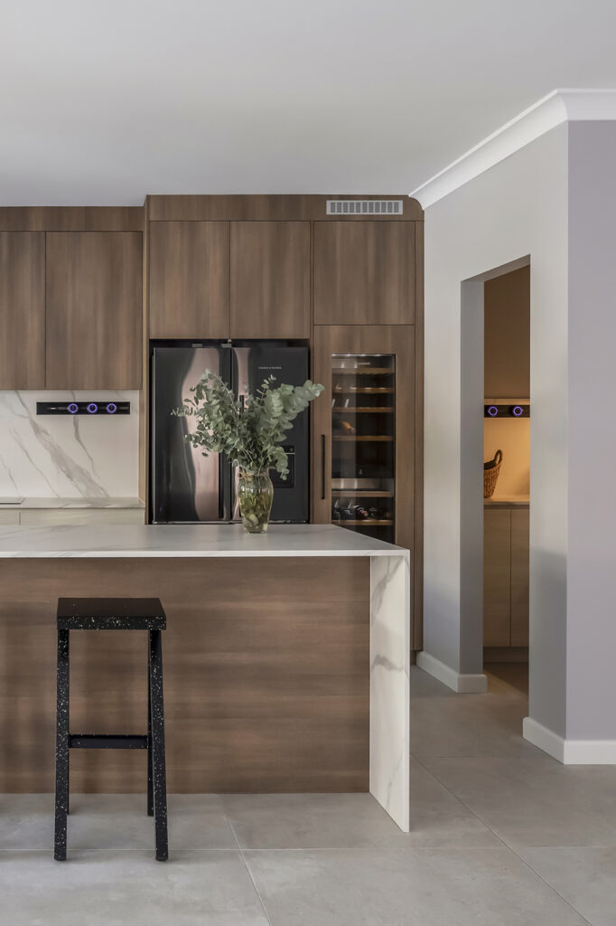 A custom wood-finish kitchenbuilt by Hoverco, featuring a marble island, black appliances, and stylish lighting.